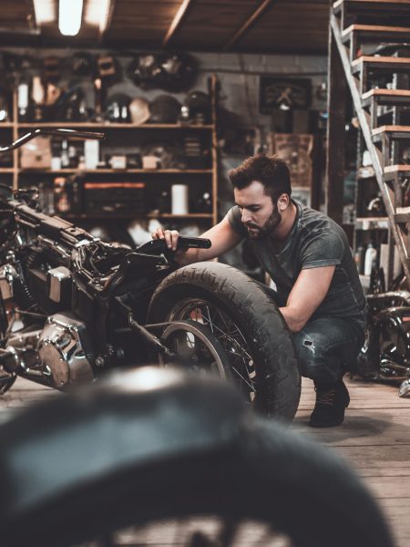Man repairing bike. Confident young man repairing motorcycle in repair shop