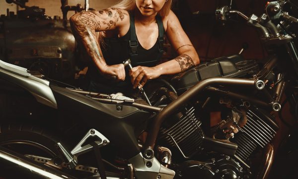 Young attractive blond woman mechanic cropped person view repairing motorcycle in workshop. Professional occupation and lifestyle concept